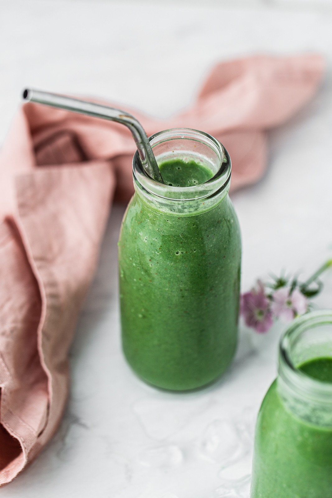 green kale smoothie in a glass with a straw