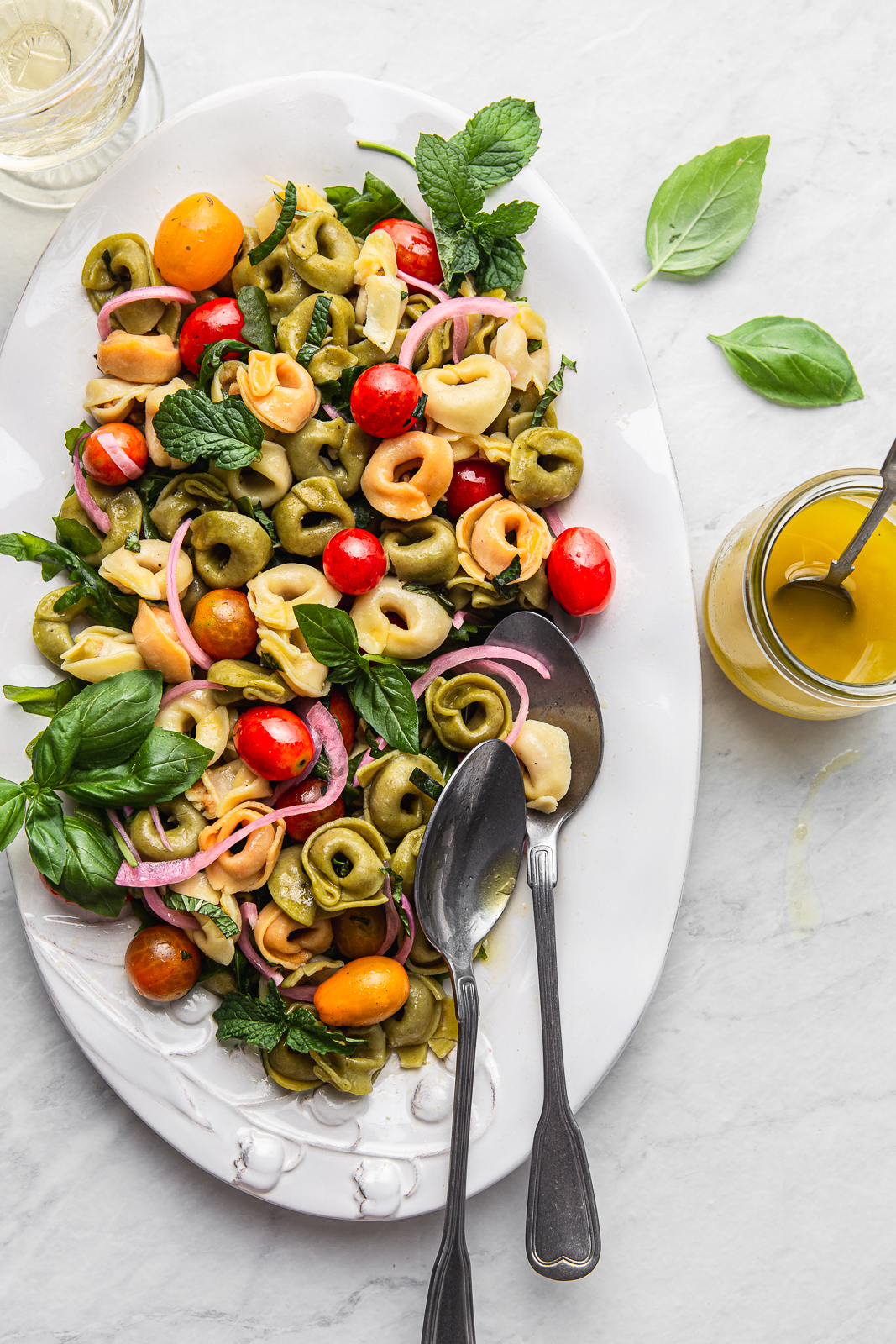 colorful tortellini pasta with cherry tomatoes, basil, red onion and vinaigrette on a white oval plate photography