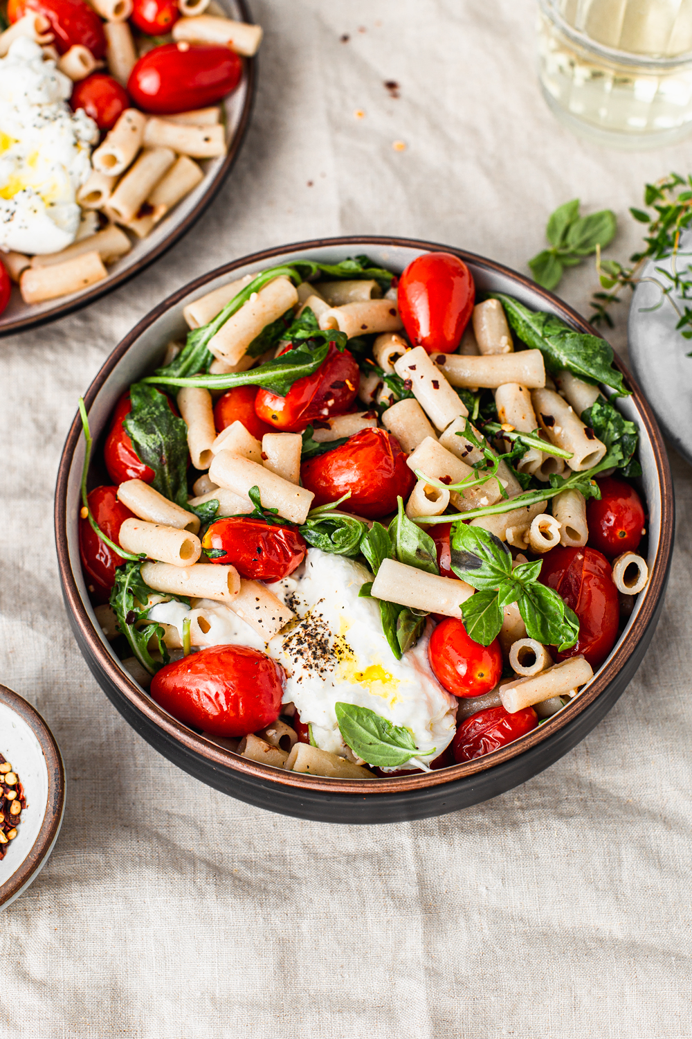 pasta bowl with cherry tomatoes basil arugula and burrata cheese with a glass of wine