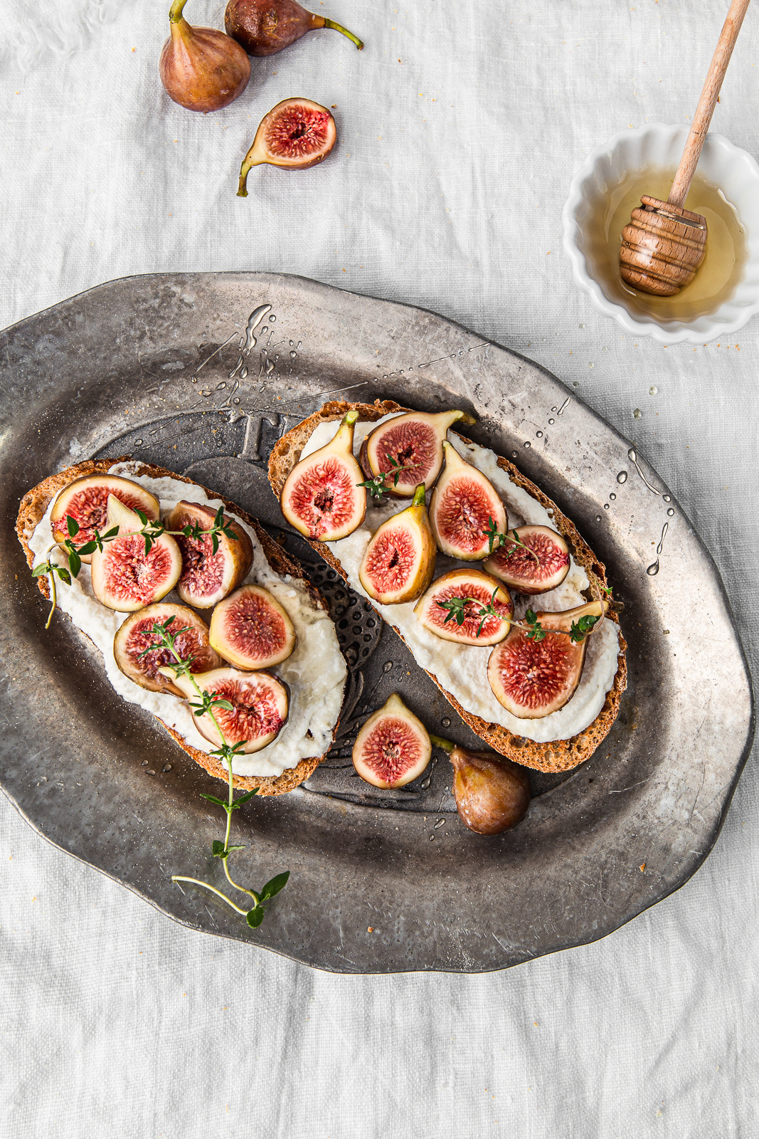 sourdough fig toasts with almond cream cheese on a silver platter with drizzle of honey
