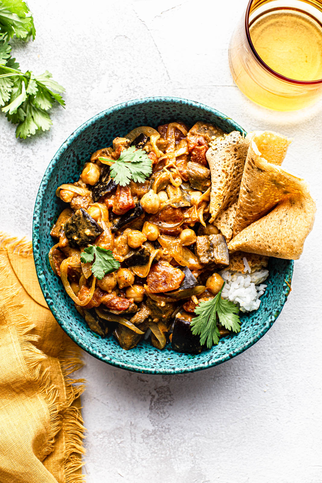 bowl of eggplant curry with chickpeas herbs white rice and chickpea pancake photography