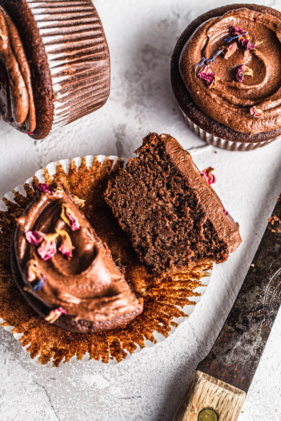 chocolate cupcakes cut in half with chocolate frosting and rose petals